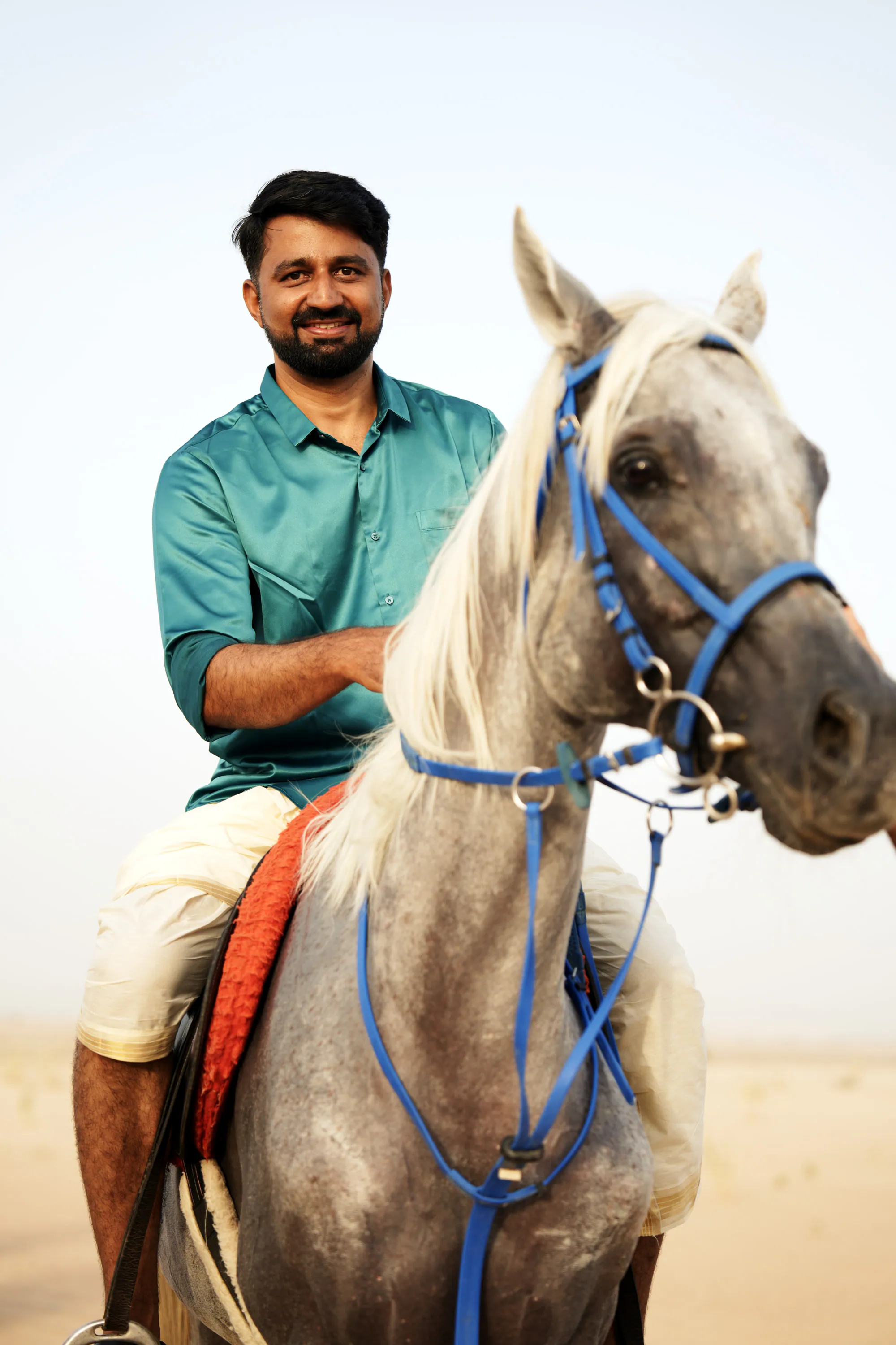 A smiling rider in a teal shirt on a grey horse with a blue bridle