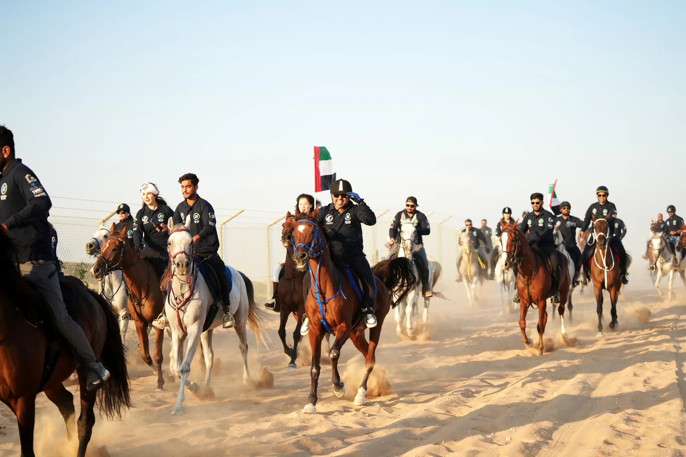 Riders cantering across the sand towards the camera with UAE flags