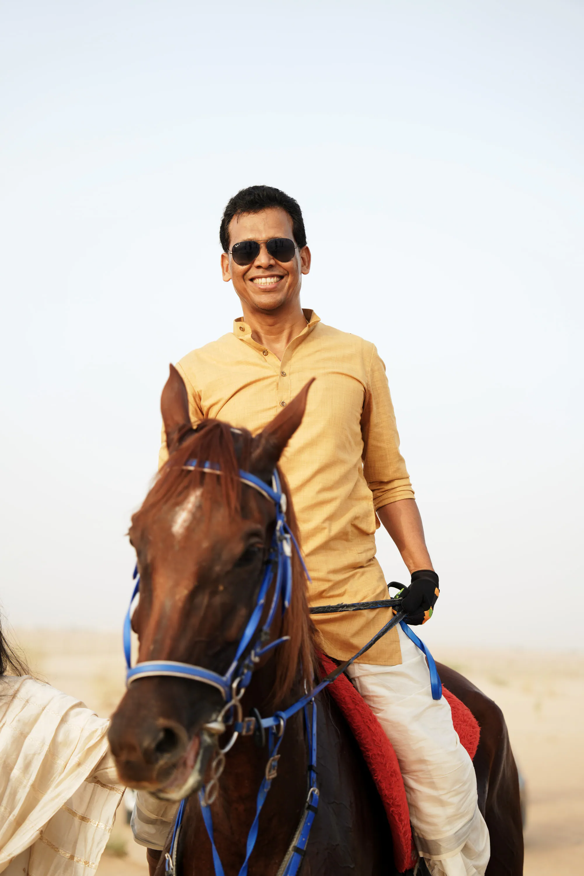 A smiling rider in a yellow shirt on a chestnut horse with a blue bridle